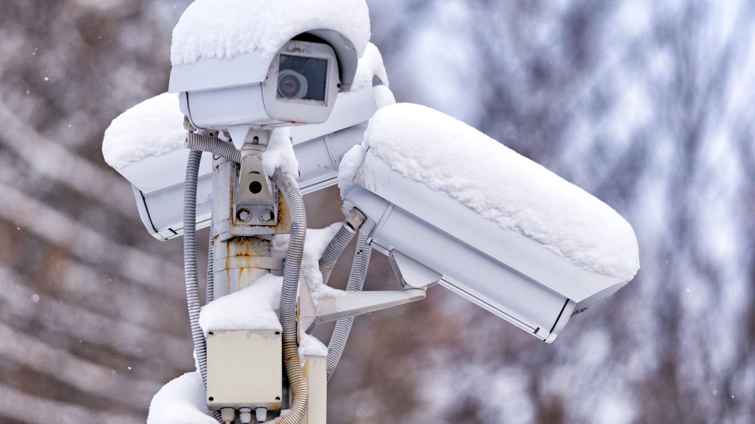 street outdoor surveillance cctv camera on stand exterior closeup view with white snow cap cold season winter blurred background